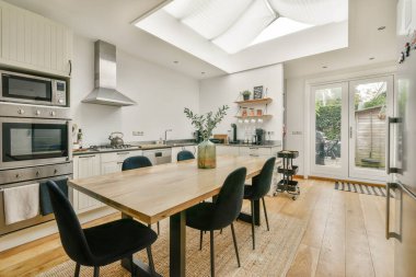 Parlak ve havadar bir modern mutfak. Yemek masası, parlak aletler ve tavan penceresinden yansıyan doğal ışıklandırmayla donatılmış minimalist bir dekor..