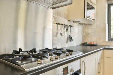 Gelişmiş aletlerin, modern bir gaz ocağının ve ev yemeklerinde fonksiyonel zarafeti vurgulayan çağdaş bir dolabın yer aldığı şık bir mutfak..