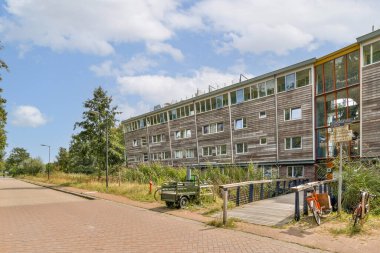 Geniş pencereli çağdaş bir apartman, yeşil ağaçlar ve açık alanların arasına yerleşmiş, davetkar bir yerleşim ortamı ve kentsel bağlantı sergiliyor..