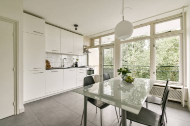 Gösterişli bir mutfak, cam bir yemek masası ve geniş pencereli davetkar bir atmosfer yaratan geniş bir mutfak..