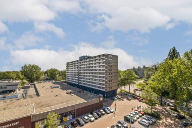 Yeşillik ve mavi gökyüzünün ortasında modern binaların yer aldığı çağdaş bir şehir manzarası mimari ve doğanın bir karışımını sergiliyor..