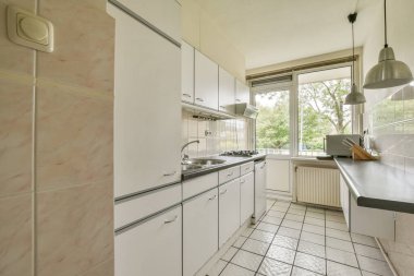 Beyaz dolap, döşeme döşemesi, geniş pencereler ve doğal ışığı karşılayan minimalist bir tasarıma sahip parlak ve havadar modern mutfak..