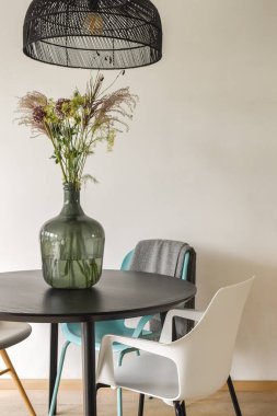 Cam vazoda çiçek aranjmanı olan yuvarlak bir masa ve yumuşak renklerde çağdaş sandalyeler içeren şık bir modern yemek düzeni..