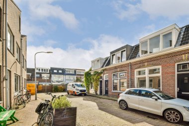 Bisikletlerin, park edilmiş arabaların ve açık gökyüzünün altında geniş pencereleri olan modern binaların yer aldığı çağdaş bir şehir merkezi manzarası.