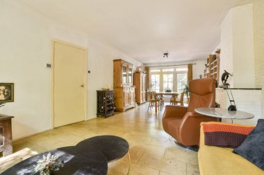 Konforlu bir sandalye ve yemek salonunun olduğu davetkar bir oturma odası. Geniş pencerelerden içeri ışık yayılıyor. Sıcak, ev gibi bir atmosfer ahşap mobilyalarla yaratılır..