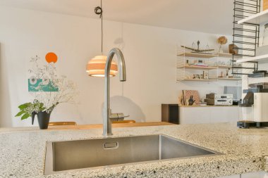 Şık kolye ışıkları, şık bir lavabo ve sanatsal duvar dekorunun yer aldığı çağdaş bir mutfak yemek ve yemek pişirmek için sıcak, davetkar bir atmosfer yaratıyor..