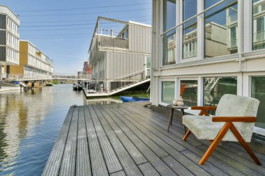 Sakin bir kanala bakan ahşap bir güvertesi olan modern bir ev mimari zarafet ve sakin su manzarası sergiliyor..