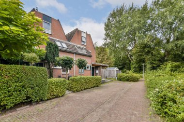 Yeşillik ve bakımlı çalılarla çevrili, girişe giden sakin bir patikayla tamamlanmış, büyüleyici bir tuğla ev manzarası..