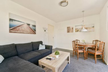 Rahat gri bir kanepe, ahşap mobilyalar ve zarif duvar sanatının olduğu şık bir oturma odası. Doğal ışık, uzayın rahat atmosferini arttırır..