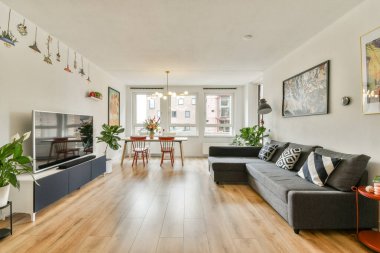 Rahat bir kanepe, yemek masası, duvar sanatı ve saksı bitkilerinin olduğu modern bir oturma odası. Uzay, çağdaş estetiği ve samimi titreşimleri yansıtıyor..