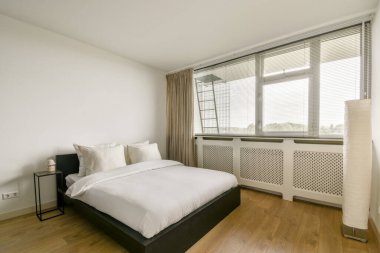 Geniş, modern bir yatak odası, düzgün yapılmış bir yatak odası, katıksız perdeli geniş pencereler, ve minimal dekor. Sıcak ahşap zemin dingin atmosferi arttırır..