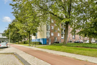 Ağaçlarla kaplı, modern apartmanların ve park edilmiş arabaların bulunduğu yerleşim yerlerinin manzaralı bir manzarası. Şehir ortamında sakin bir atmosfer..