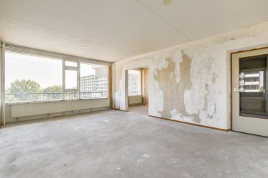 Geniş pencereli, dekorasyon ve mobilya için hazırlanmış boş bir odayı gösteren çıplak bir oda. Duvarlar görülebilir dokularla kısmen tamamlanmamış..