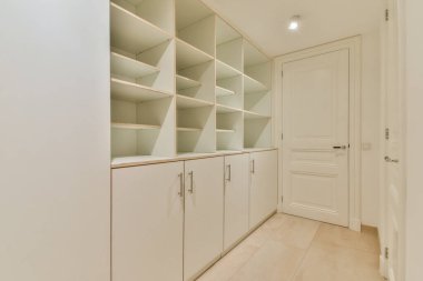 Minimalist raf ve dolapların yer aldığı gösterişli, modern bir iç mekan. Temiz çizgiler ve nötr renkler organizasyon için mükemmel bir sakinleştirici atmosfer yaratır..