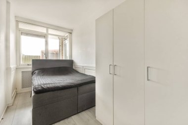 Temiz ve basit bir yatak odası parlak bir duvara karşı bir yatak sergiliyor. Beyaz mobilyalar, doğal ışığın içeri aktığı sakin atmosferi tamamlıyor..