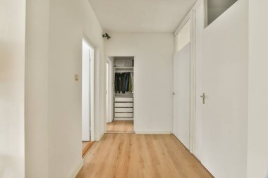 Beyaz duvarların ve ahşap zeminin olduğu minimalist bir koridor, dolaba açılıyor, modern iç tasarım estetiğine örnek olarak..