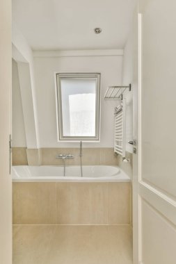 İçinde küvet, gösterişli eşyalar ve doğal ışık için geniş bir pencere olan modern bir banyo. İç tasarım temizliği ve basitliği vurguluyor..