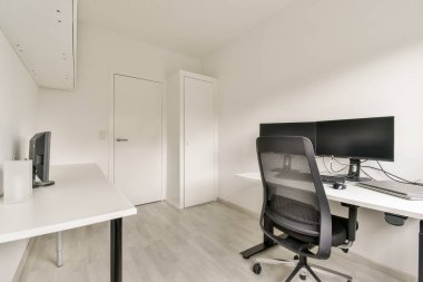 Bir masa, ergonomik sandalye ve bilgisayar monitörünün yer aldığı şık ve düzenli bir ofis. Uzay, temiz ve minimalist estetiği vurguluyor..