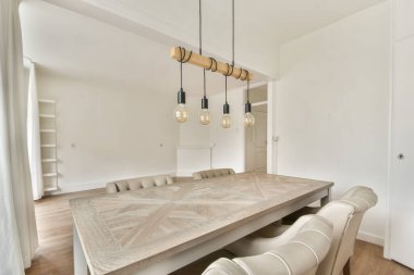 Ahşap bir masa ve tavandan sarkan kendine özgü kolye ışıklarının olduğu modern bir yemek odası davetkar bir atmosfer yaratıyor..