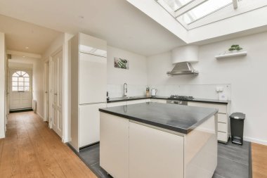 Gösterişli, modern bir mutfak, minimalist tasarım, beyaz dolaplar, merkezi bir ada, ve geniş doğal ışık pencereleri..