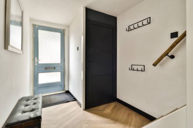 Zarif mavi bir kapı, minimalist bir dekor ve çekici duvar kancalarının yanında şık siyah bir bank içeren şık ve modern bir giriş koridoru..