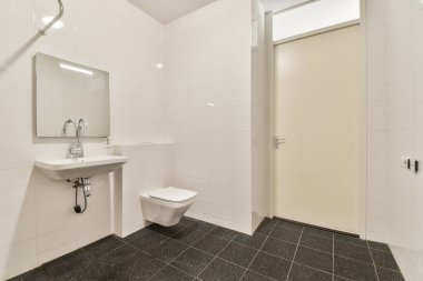 Bu resim, beyaz kiremitler ve tek renkli zemin de dahil olmak üzere minimalist tasarım özelliklerine sahip gösterişli ve modern bir banyo sergiliyor. Alan işlevselliği ve biçimi vurgular.