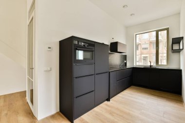Gösterişli siyah dolap ve minimalist tasarım elementleri, odayı doğal ışığın doldurmasına izin veren geniş pencereli bu çağdaş mutfak alanını tanımlar..