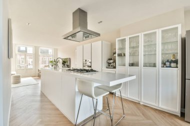 Beyaz dolaplar, bir ada ve doğal ışık için geniş pencereleri olan gösterişli ve çağdaş bir mutfak. Modern yaşam alanları için ideal.