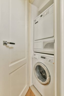 Düzgünce düzenlenmiş bir çamaşırhane. Üst üste yığılmış çamaşır makinesi ve kurutma makinesinin olduğu bir dolap. Temiz çizgiler ve parlak renk işlevsel bir alan yaratır.