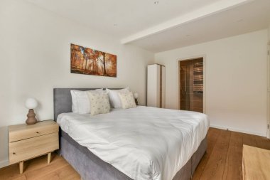 Rahat bir yatak odası, yumuşak çarşaflar ve şık bir komodinin olduğu gösterişli, minimalist bir yatak odası. Doğal ışık sakin atmosferi güçlendirir..