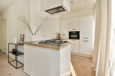 Parlak ve çağdaş bir mutfak. İçinde gaz ocağı, beyaz dolaplar ve doğal ahşap aksanlar var. Yer parlak ve cezbedici, minimalist dekoruyla.