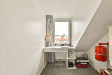 Kompakt çalışma alanı modern bir masa, doğal ışık getiren bir pencere ve temiz ve düzenli bir ortam için minimum dekor içerir..
