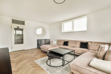 Rahat bir kanepe, sehpa ve doğal ışığa izin veren geniş pencereli modern bir oturma odası. Ahşap döşeme boşluğa sıcaklık katıyor..