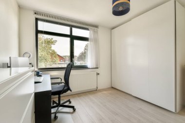 Pürüzsüz bir masa, rahat bir sandalye ve doğal ışık için geniş bir pencereye sahip temiz ve parlak bir ofis, davet edici bir çalışma alanı ortamı yaratıyor..