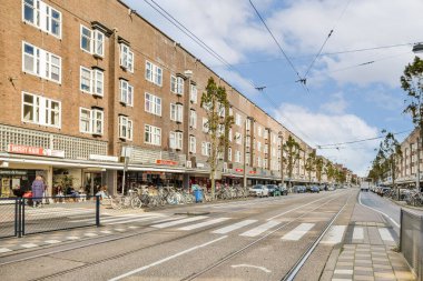 Birden fazla bina, dükkan ve açık hava oturma yerlerinin bulunduğu hareketli bir şehir caddesi. Bisikletler cadde boyunca diziliyor, mimari ve şehir hayatının bir karışımını sergiliyorlar..