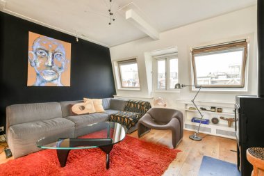 Benzersiz bir duvar sanat eseri, rahat gri bir kanepe ve modern mobilyaların bulunduğu modern bir oturma odası rahat ama şık bir atmosfer yaratıyor..