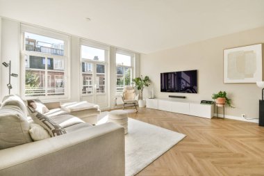 Şık mobilyaların, doğal ışığa izin veren geniş pencerelerin ve minimalist estetiğin bulunduğu çağdaş bir oturma odası. Rahatlama ve toplanma için ideal..