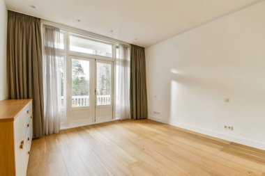 Doğal ışığı, minimalist mobilyaları ve sıcak ahşap zemini davet eden geniş pencereli parlak, havadar bir oda, sakin bir atmosfer yaratıyor..