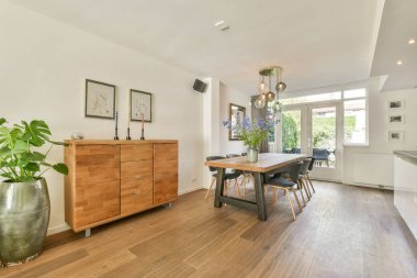 Ahşap mobilyalar, dekoratif bitkiler ve doğal ışıklandırmadan oluşan modern bir yemek odası. Toplantılar için sıcak ve davetkar bir atmosfer yaratıyor..