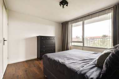 Gösterişli ve modern bir yatak odası tasarımı, minimalist mobilyalar, doğal ışık için geniş pencereler, ve rahatlamayı teşvik eden samimi bir estetik..