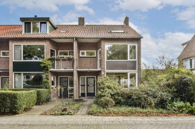 Modern ve geleneksel tasarımların bir karışımını sunan zarif çok katlı bir ev, yemyeşil ve berrak bir gökyüzü ile çevrili..