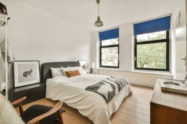 Geniş pencerelerden gelen doğal ışık, nötr renkler ve sakin bir atmosfer için minimalist dekorlar içeren iyi tasarlanmış modern bir yatak odası..