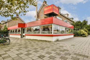 Parlak kırmızı bir cephe ve yeşilliklerle çevrili büyük cam pencerelerin bulunduğu çağdaş bir restoran. Yemek ve günlük geziler için ideal..