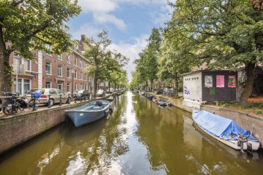 Ağaçlar ve büyüleyici binalarla kaplı, sakin suyu ve berrak gökyüzünü yansıtan, kıyılar boyunca demirlemiş teknelerle dolu pitoresk bir kanal..