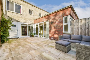 Modern mobilyaların, bakımlı bir avlunun ve doğal ışığı davet eden büyük pencerelerin bulunduğu şık bir açık hava oturma alanı..