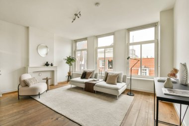 Geniş pencereleri, yumuşak halısı ve estetik ve konfor için tasarlanmış modern mobilyaları olan şık bir minimalist oturma odası..