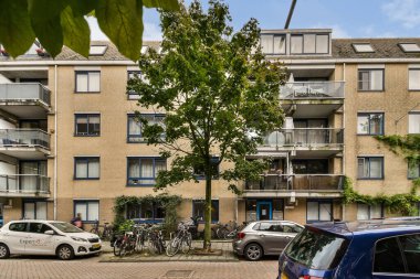 Çağdaş bir apartman kompleksi, park halindeki bisiklet ve arabalarla çevrili, canlı bir mahallede yaşayan şehirlileri gözler önüne seren birden fazla balkondan oluşuyor..