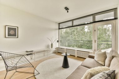 Gösterişli mobilyaların, doğal ışığa izin veren geniş pencerelerin ve minimalist bir tasarımın bulunduğu çağdaş bir oturma odası. Konforlu toplanma ya da rahatlama için ideal.