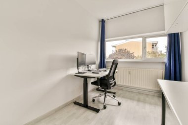 Pürüzsüz ve minimalist bir ev ofisi. İçinde bilgisayar, ergonomik sandalye ve üretkenliği destekleyen bol miktarda doğal ışık bulunan bir masa..