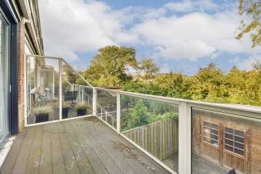 Cam parmaklıklı şık bir balkon canlı yeşillik ve doğal çevrenin davetkar bir görüntüsü, açık hava yaşam alanının vurgulanması.